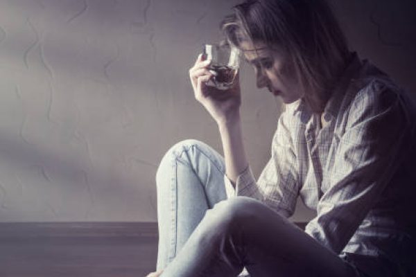 Young woman in depression drinks alcohol while sitting on the floor